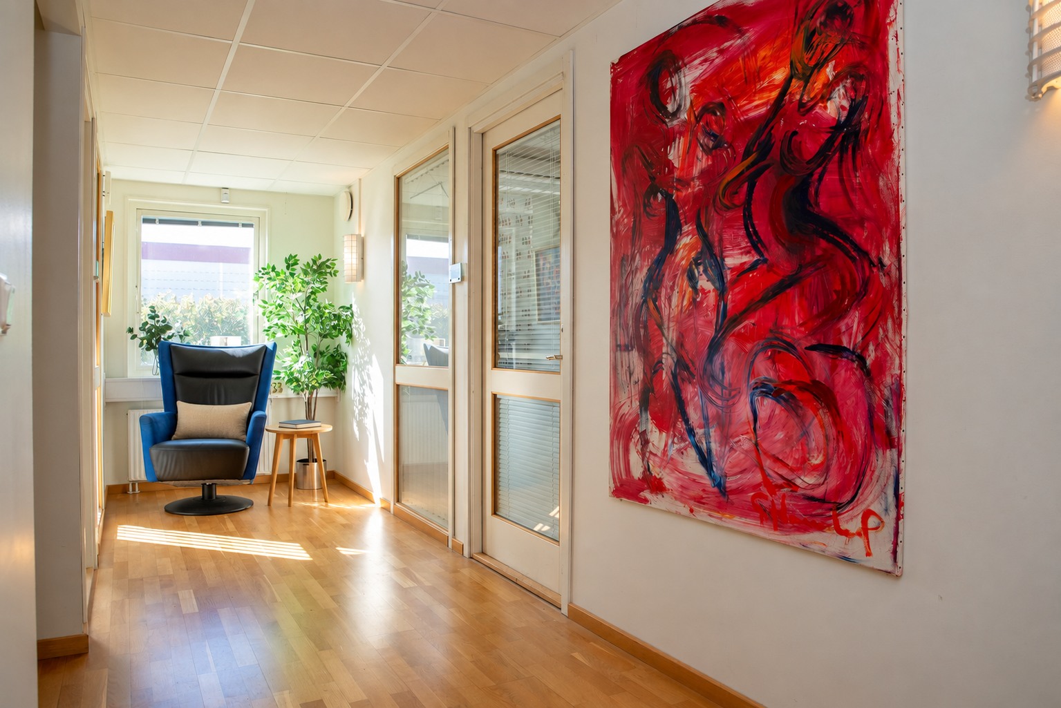 Ljus korridor vid kontorsrummen med konst och sittplats