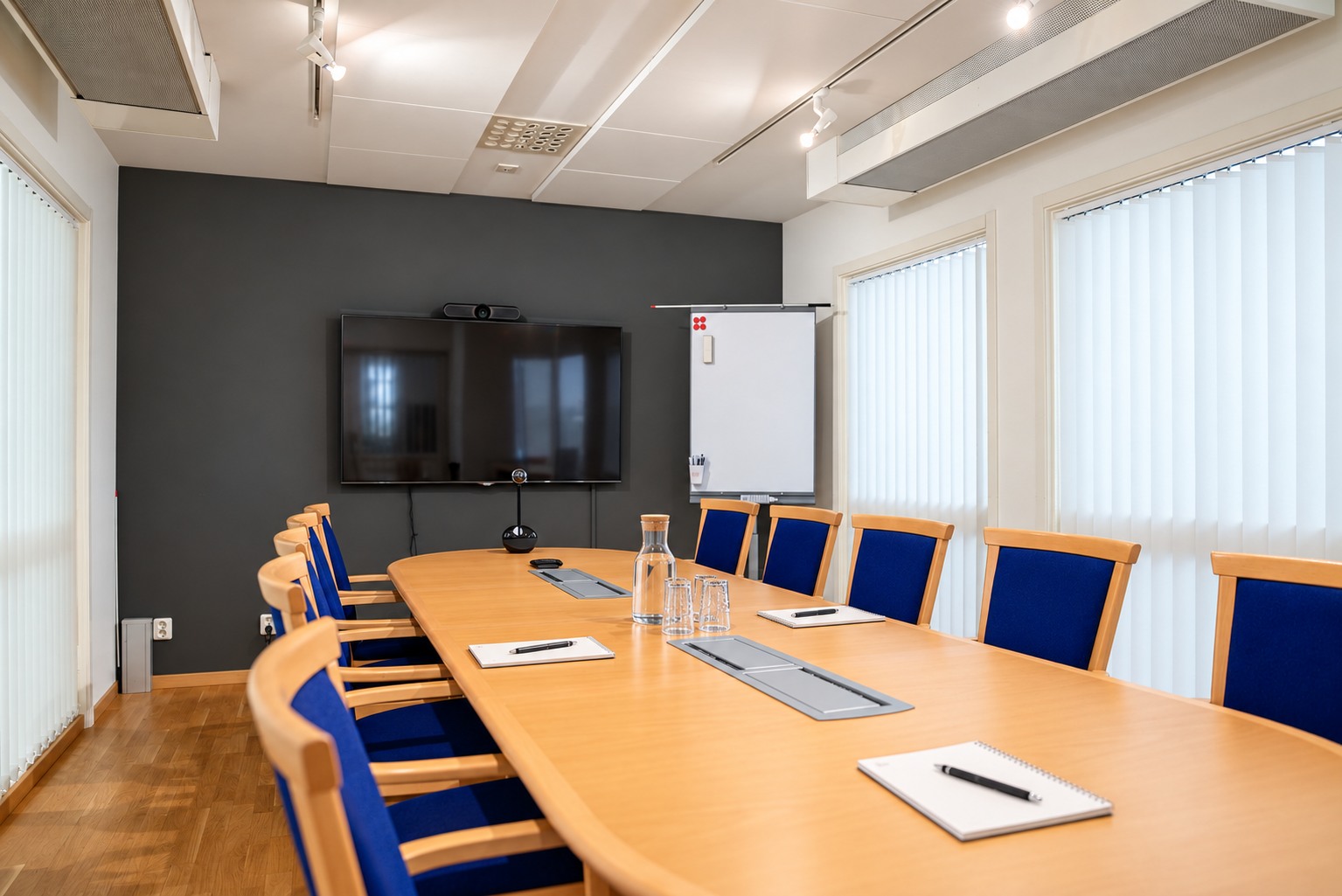 Mötesrum 2 med långt konferensbord, blå stolar, skärm och skrivtavla